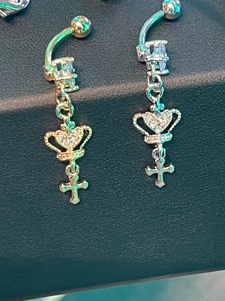 A pair of belly button rings with a heart and cross on them.