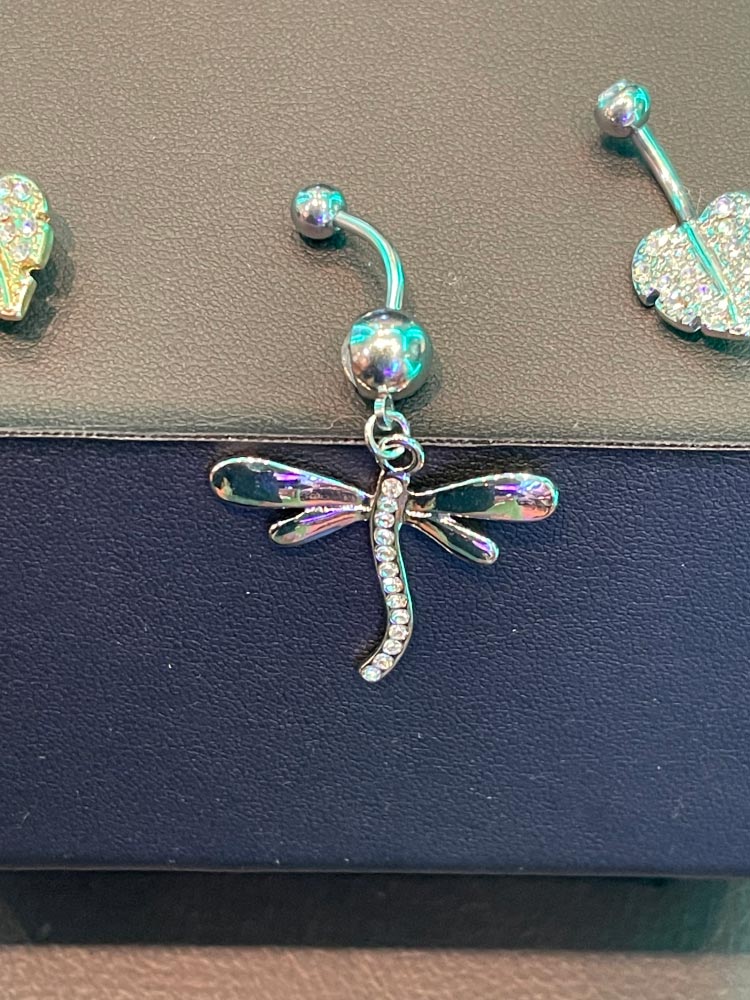 A close up of a belly button ring with a dragonfly pendant.
