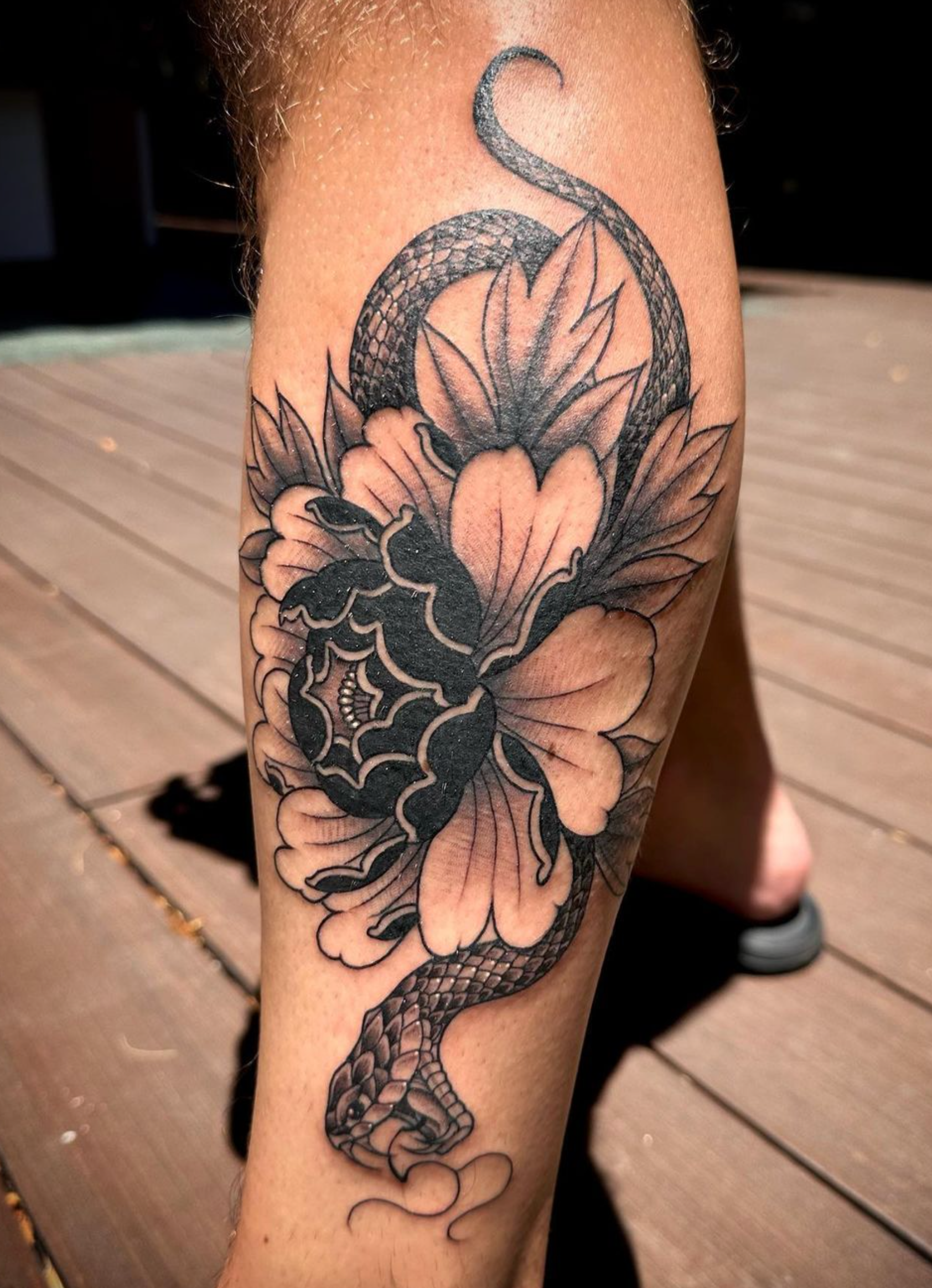 A person has a tattoo of a snake and a flower on their leg