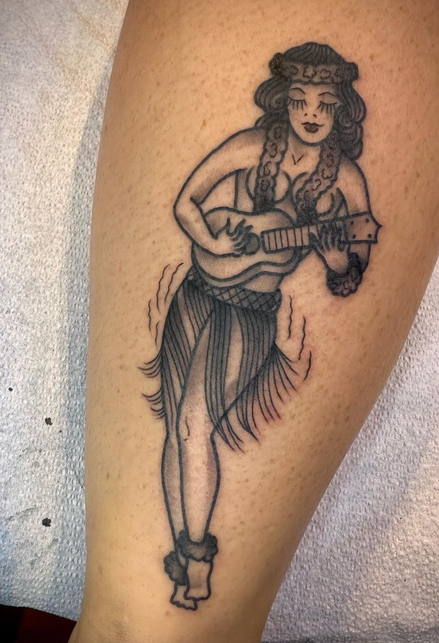 A tattoo of a woman playing an ukulele on a leg