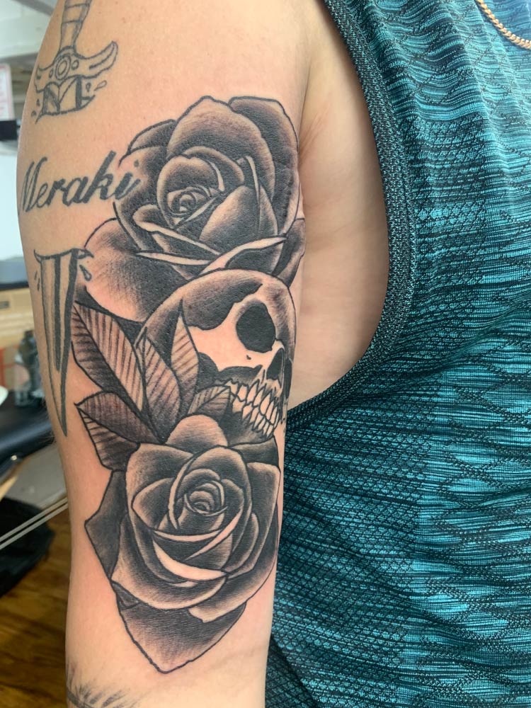 A person has a tattoo of roses and a skull on their arm.