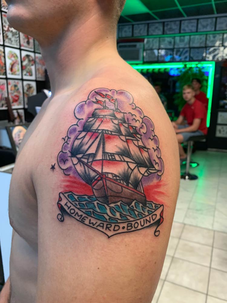 A man has a tattoo of a sailboat on his shoulder.