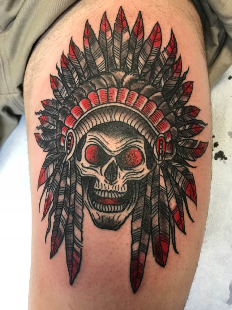 A tattoo of a skull wearing a native american headdress on a person 's leg.