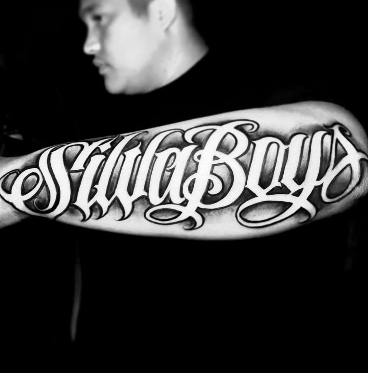 Forearm tattoo  in bold, ornamental script with intricate shading and flourishes by Ricky Pantera.