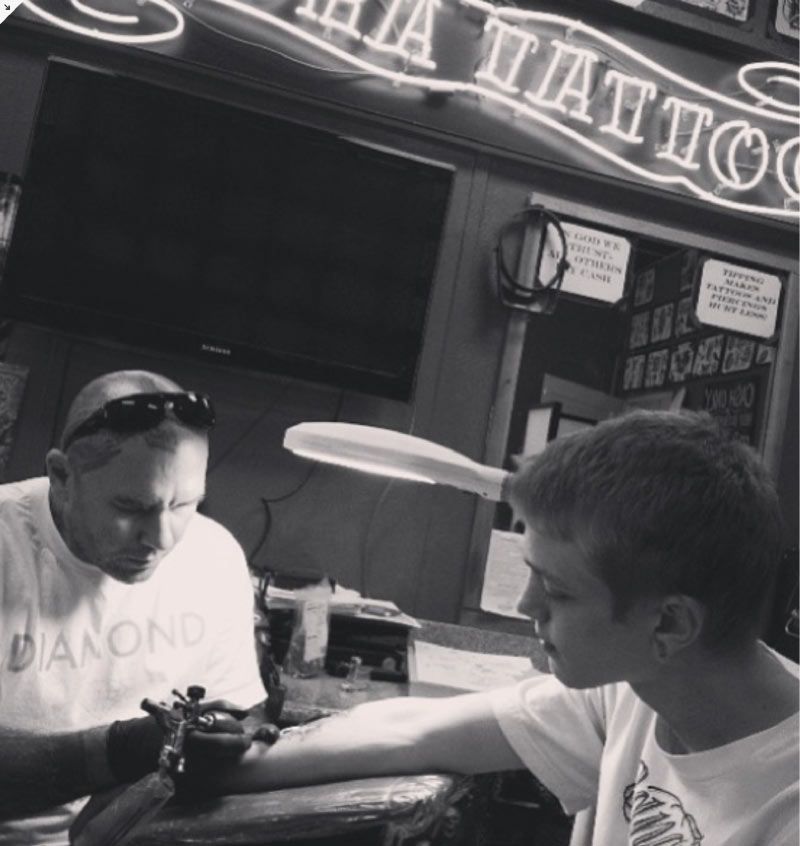 A man is getting a tattoo on another man 's arm at a tattoo shop