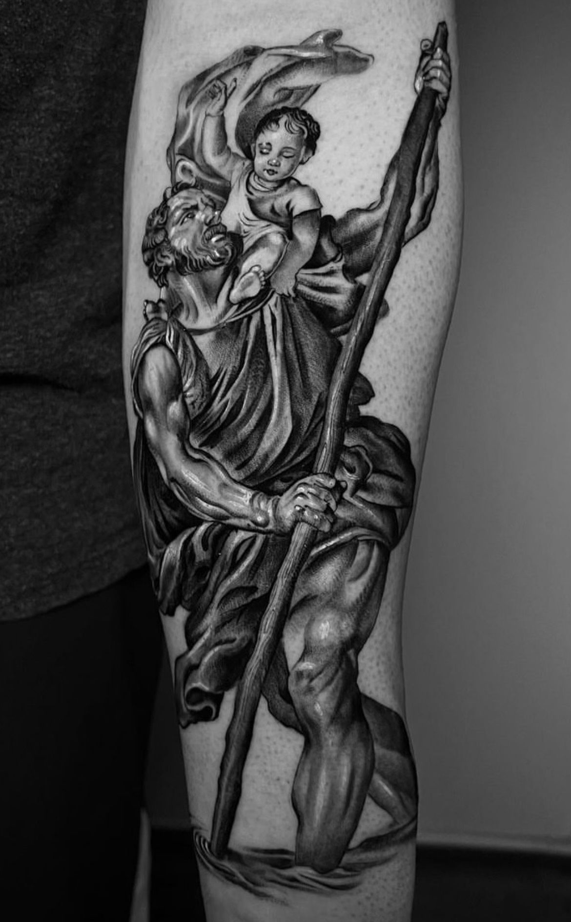 A black and white tattoo of a man holding a baby on his arm.
