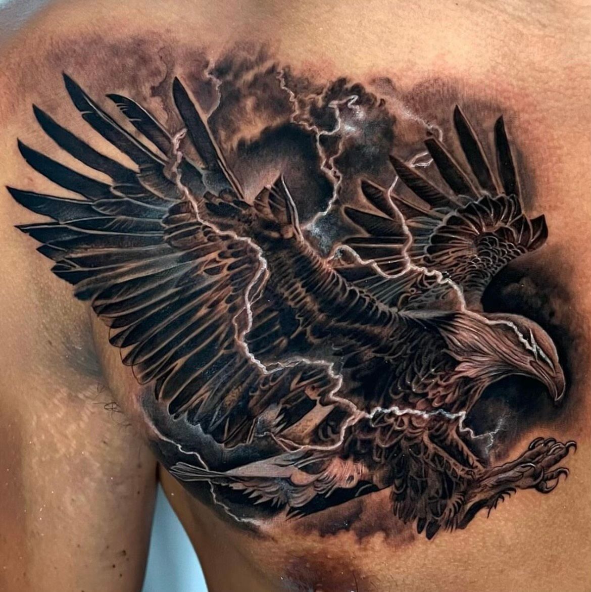 A man has a tattoo of an eagle flying through lightning on his chest.