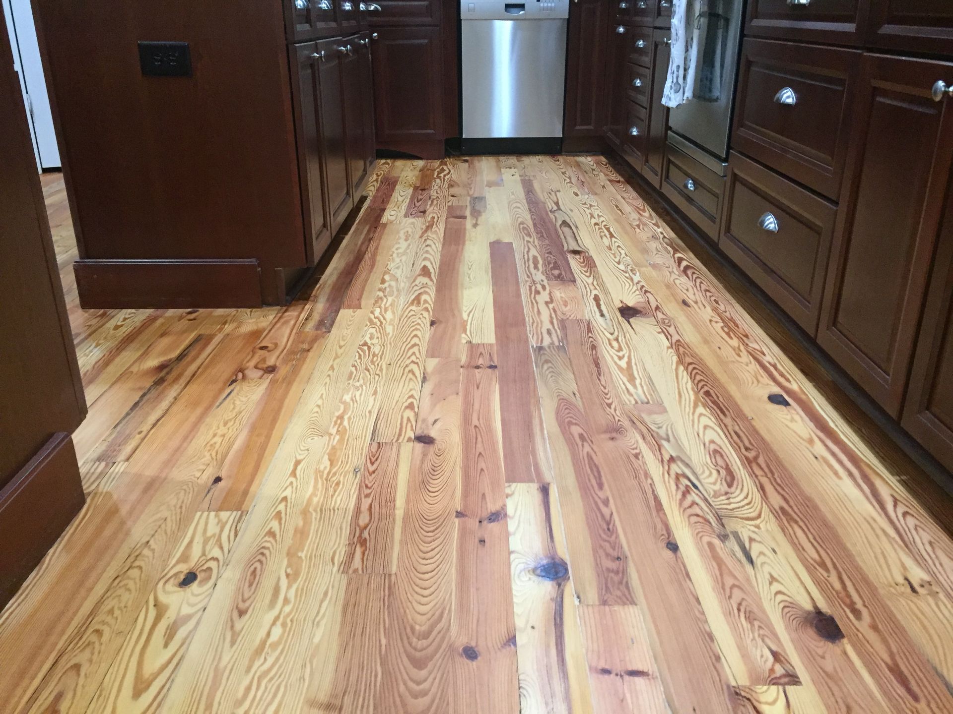 Wooden kitchen floor with dark brown cabinets and a dishwasher.