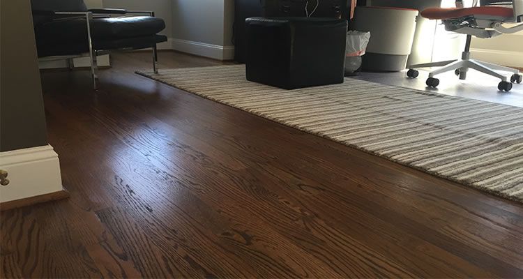 Dark wood floor with a rug and furniture in the background.