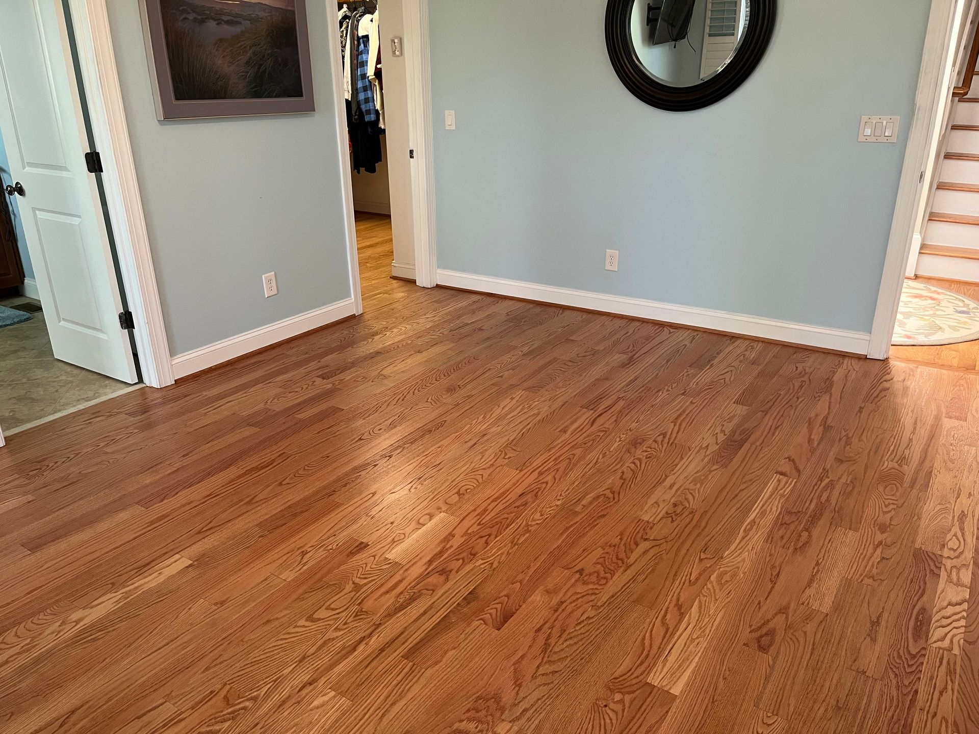 Hardwood floor in a room with light blue walls, white trim, and a round mirror.