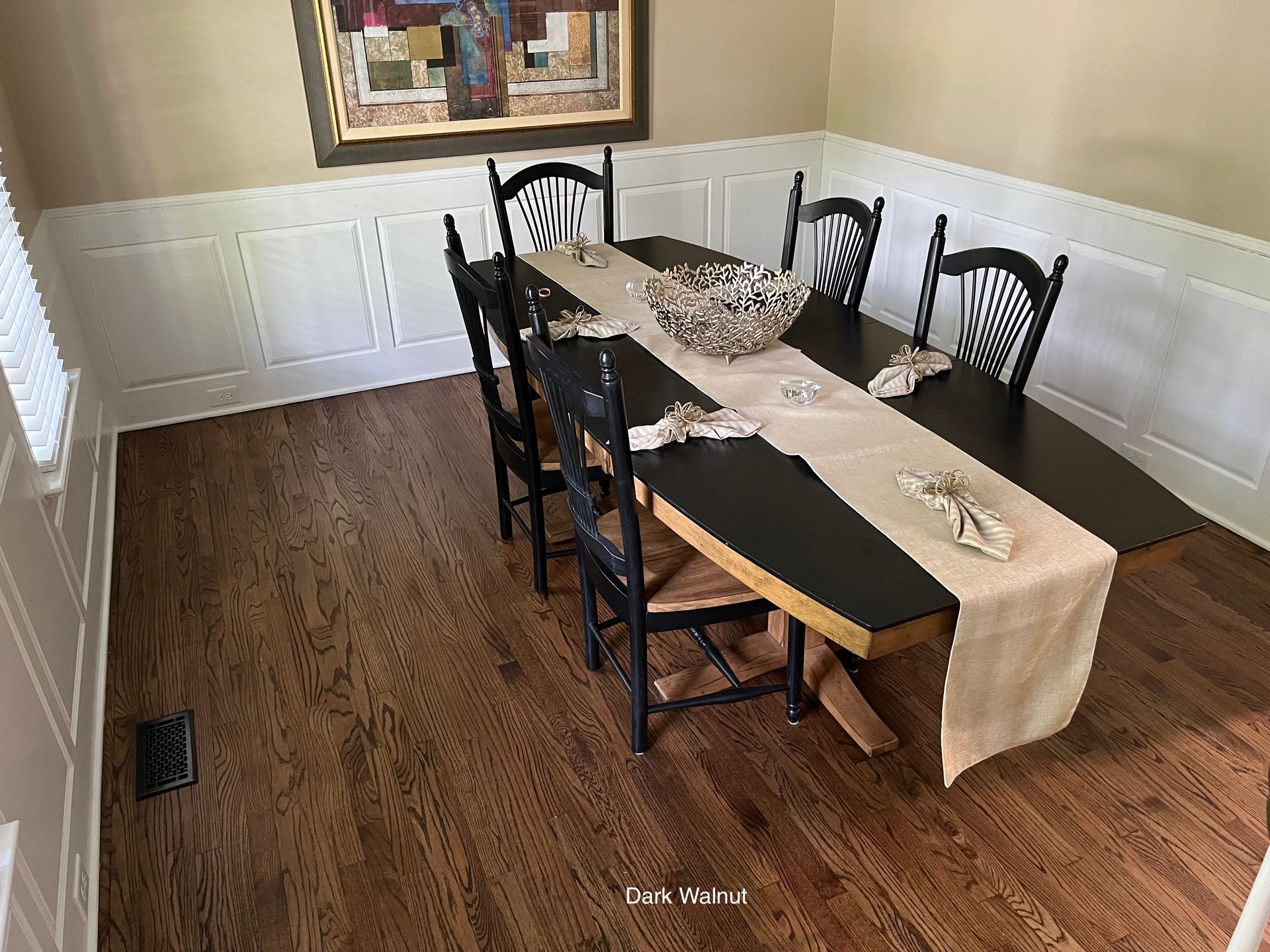 Dining room with dark wooden table, black chairs, and neutral runner. Hardwood floor and white paneling.