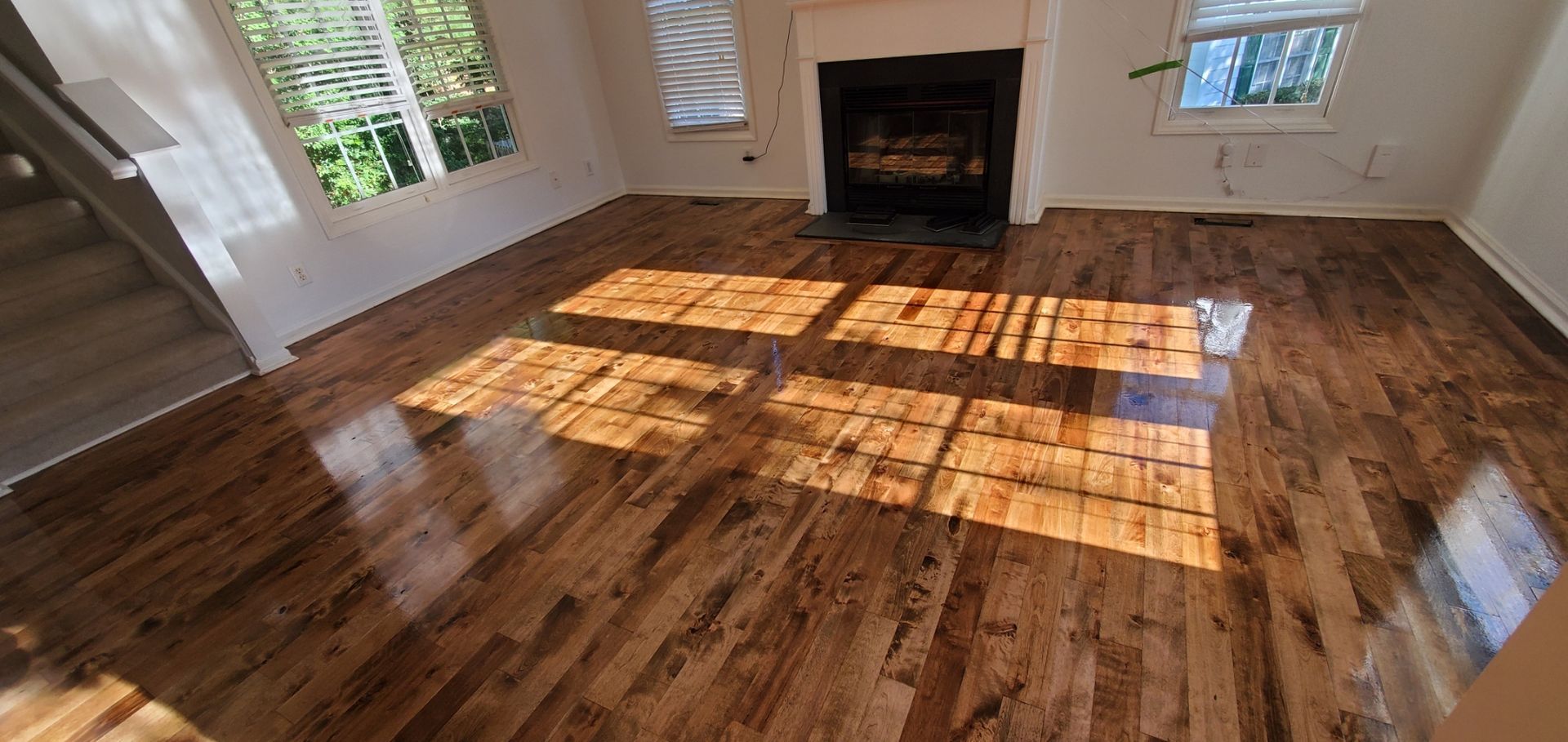 Wooden floor in a room with a fireplace and windows, sunlight casting shadows.