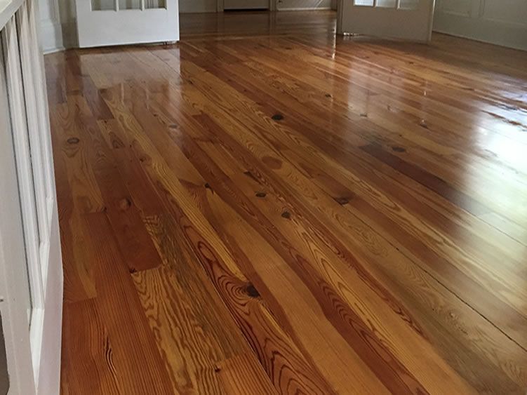Shiny, newly refinished wooden floorboards with a reddish-brown hue, reflecting light from a window.