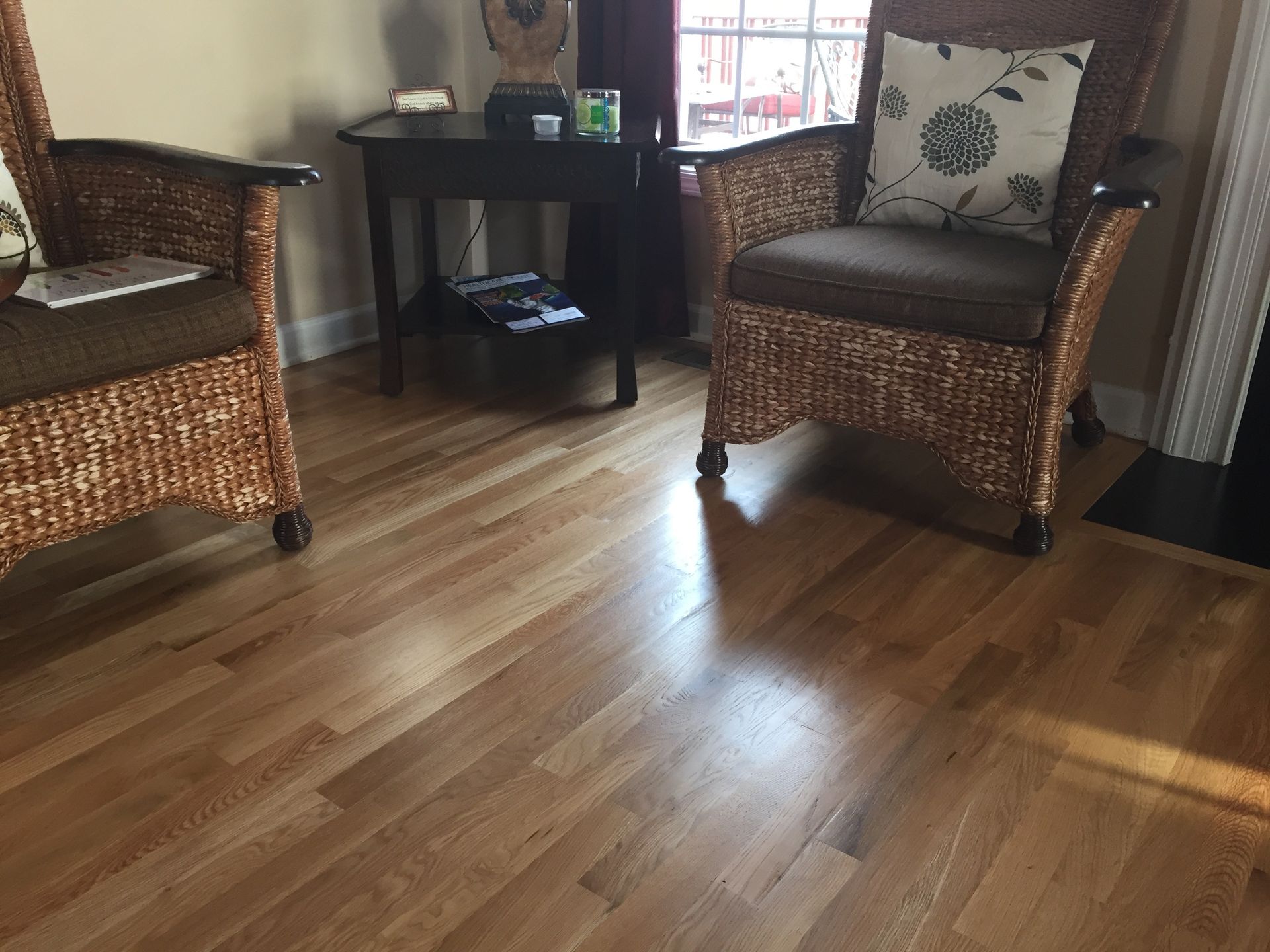Two wicker chairs, a small table, and wood flooring. A room with sunlight.
