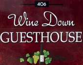 "Sign for Wine Down Guesthouse, burgundy background with white script and sans-serif text, bottle and grapes."