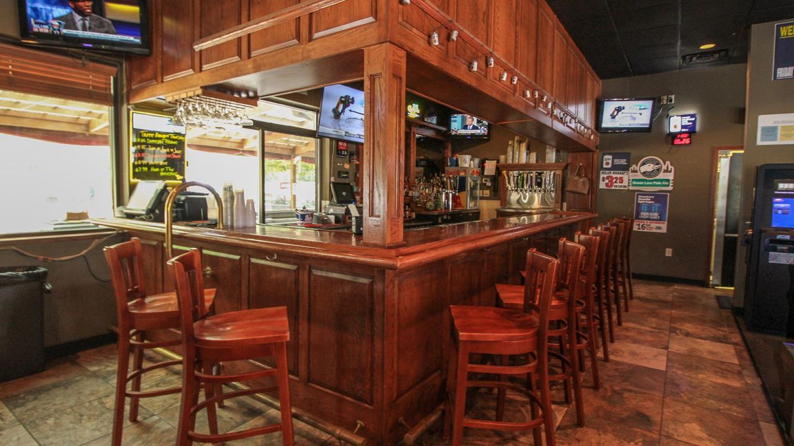 A long wooden bar with stools and televisions in a restaurant.