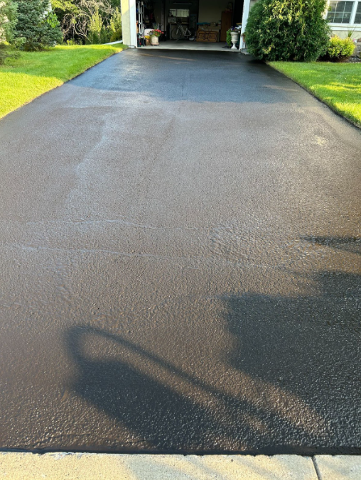 A black asphalt driveway leading to a garage and a house.