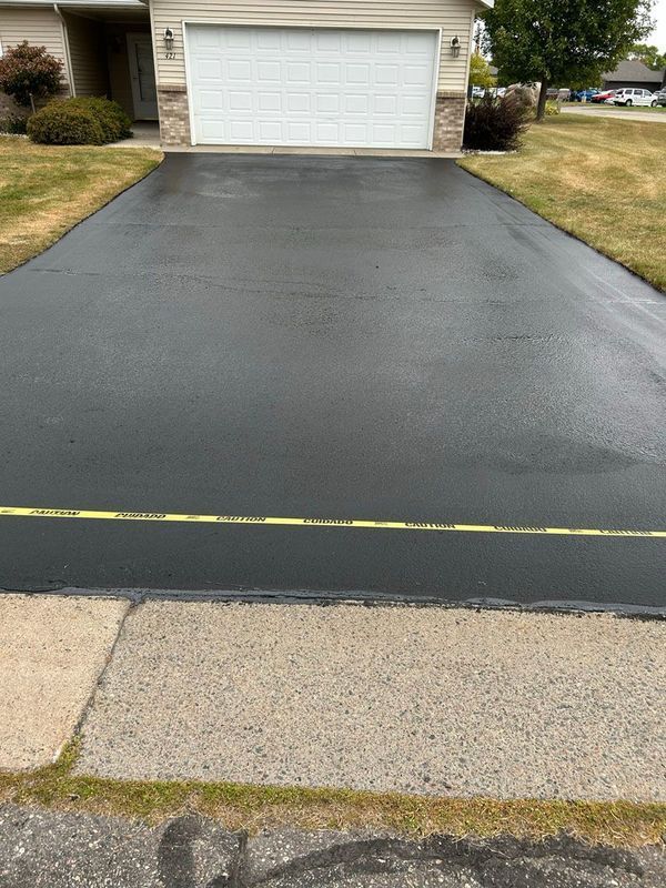A black driveway with a white garage door in front of a house.