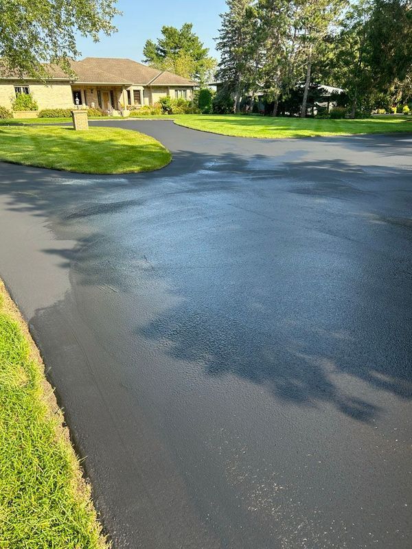 A driveway with a house in the background and trees on the side.