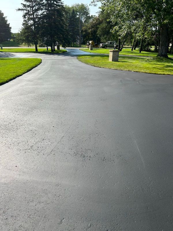 A black asphalt driveway surrounded by grass and trees