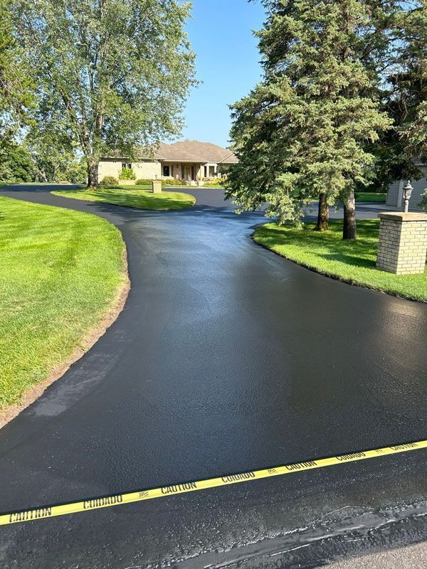 A driveway with a house in the background and trees on the side.