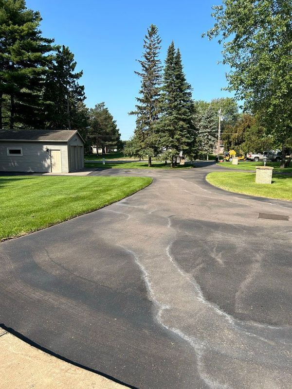 A driveway with trees on both sides and a garage in the background