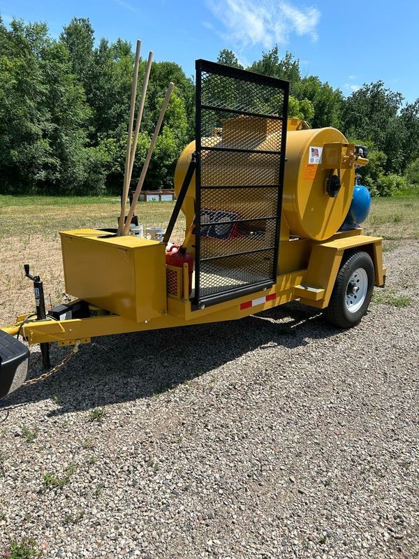 A yellow trailer with a large tank on it is parked in a gravel lot.