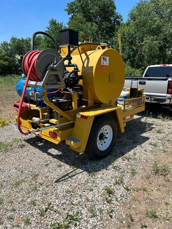 A yellow trailer with a hose attached to it is parked in a gravel lot.