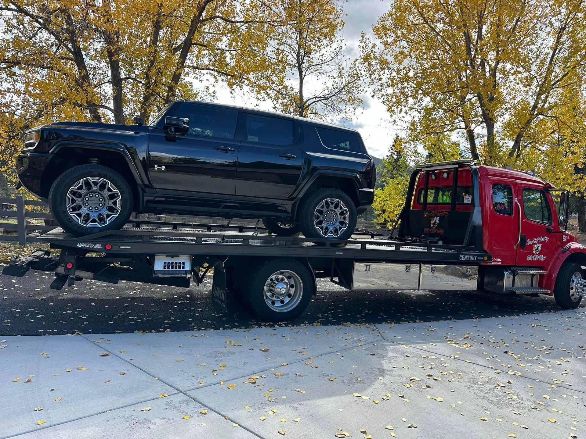 Black Hummer SUV on a red tow truck. Outdoors, on a paved area, with fall foliage.