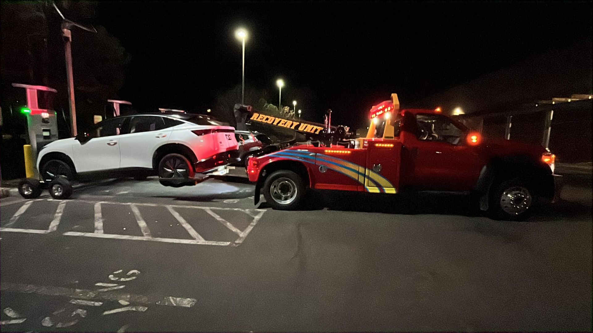 A white SUV being towed by a red tow truck at night.