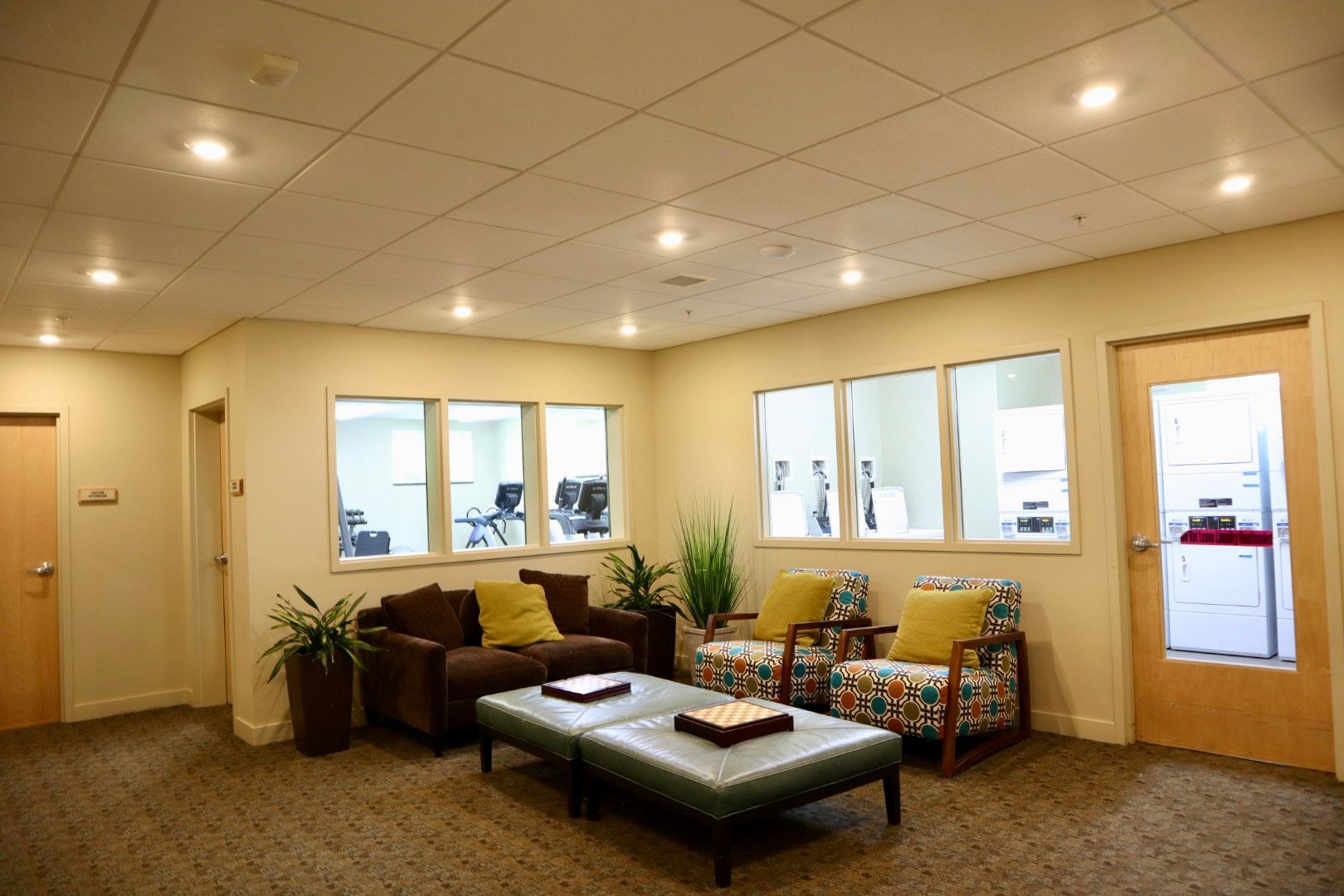 A living room with a couch , chairs , ottoman , and windows.