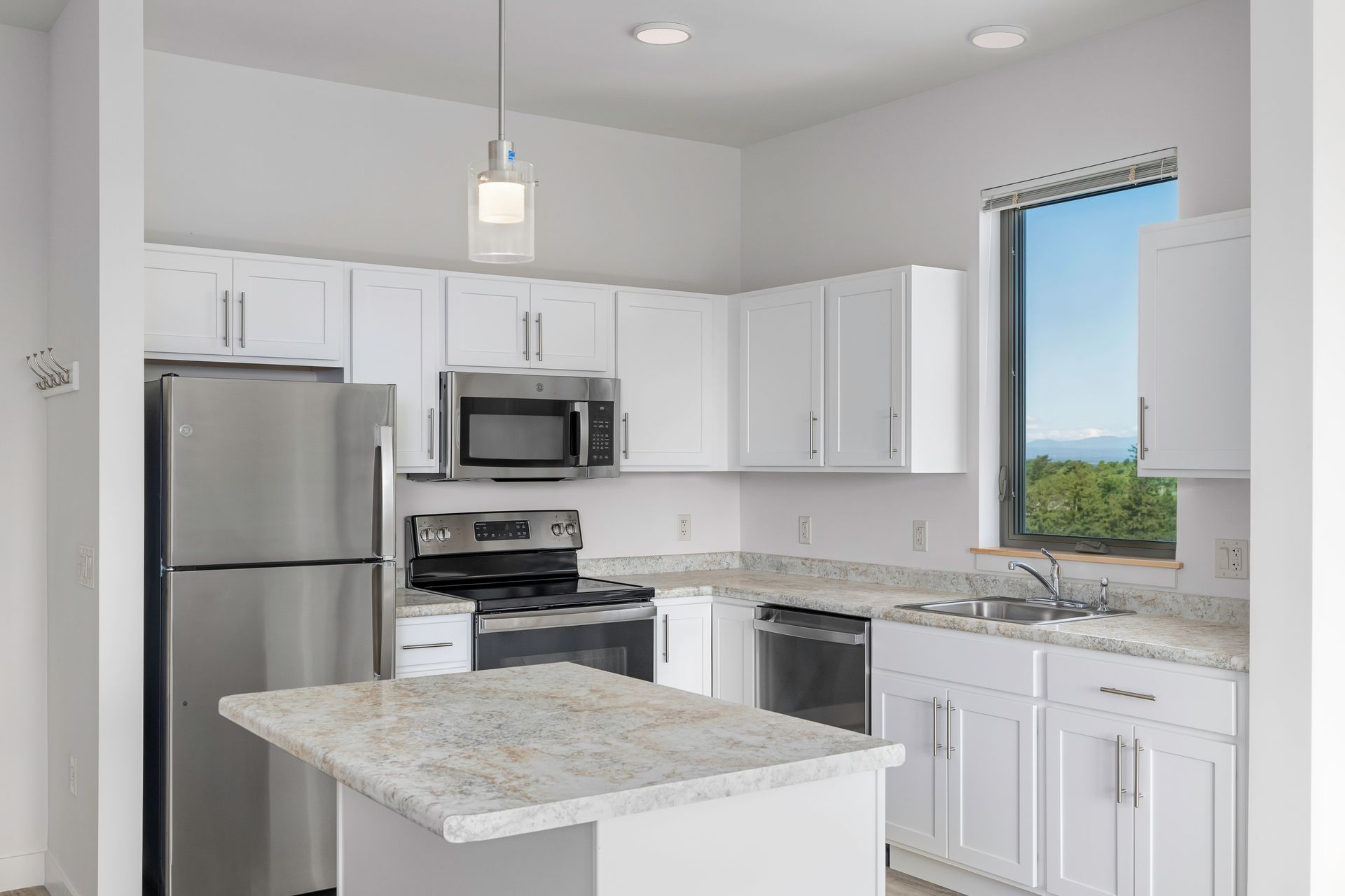 A kitchen with white cabinets , stainless steel appliances , a refrigerator , microwave and sink.