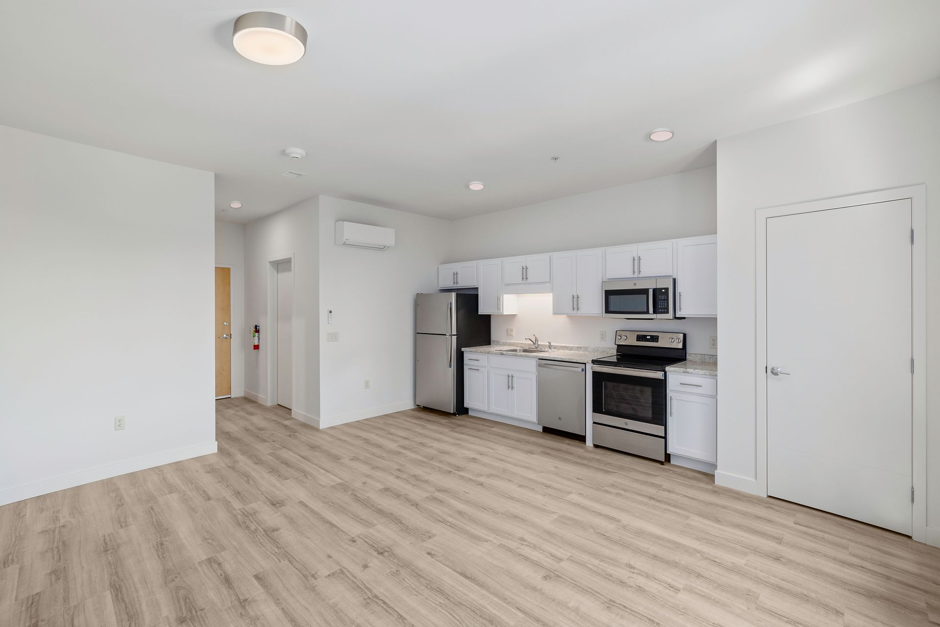 A kitchen with white cabinets , stainless steel appliances , a refrigerator and a microwave.