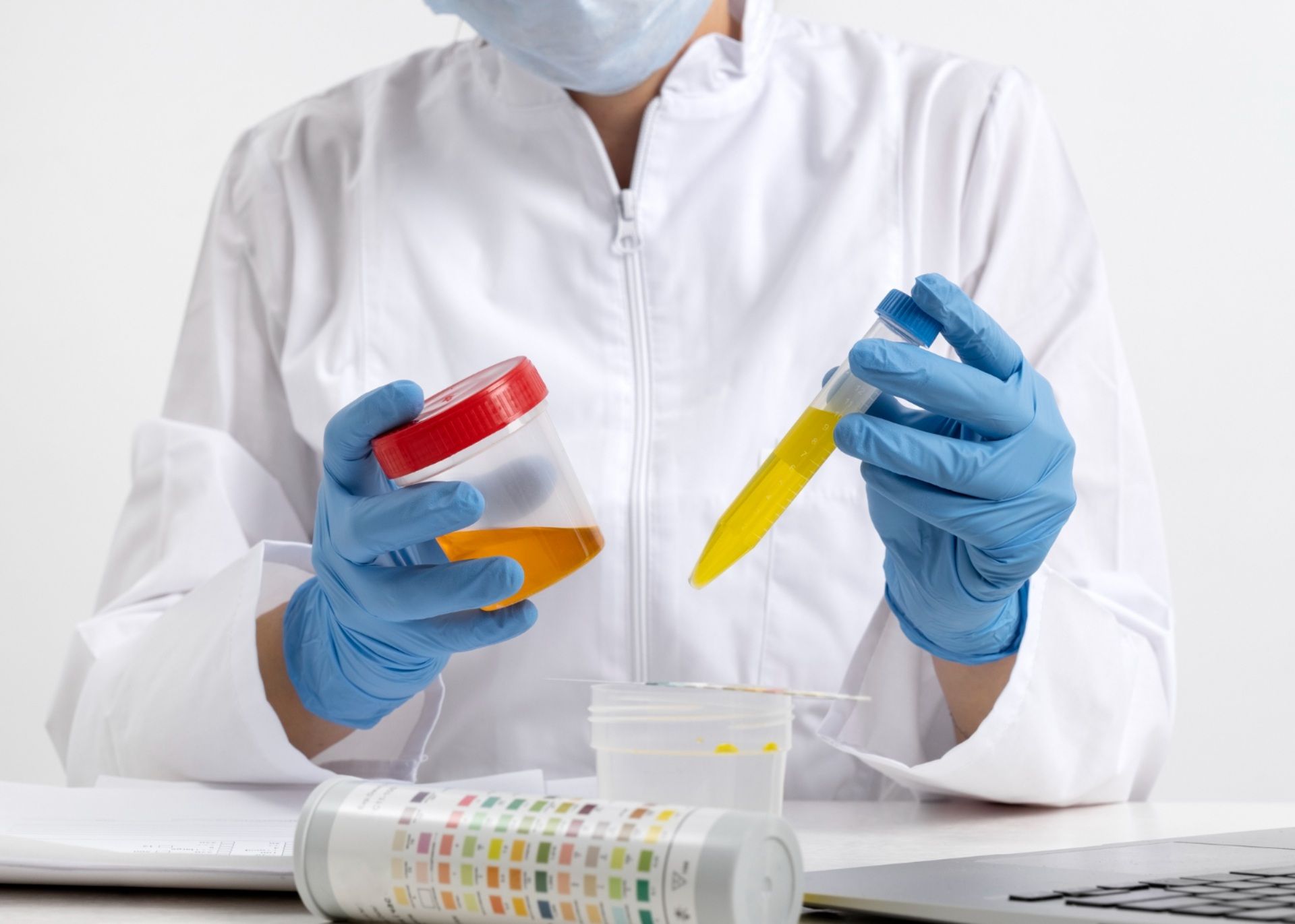 Person in lab coat and gloves holding urine sample, testing in lab setting.