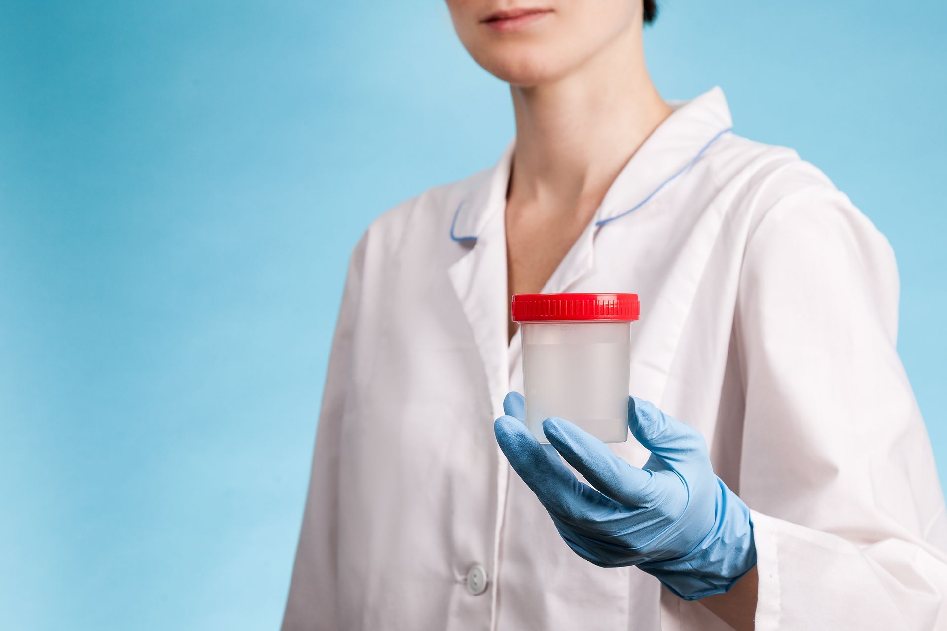 Person in lab coat and gloves holding urine sample, testing in lab setting.