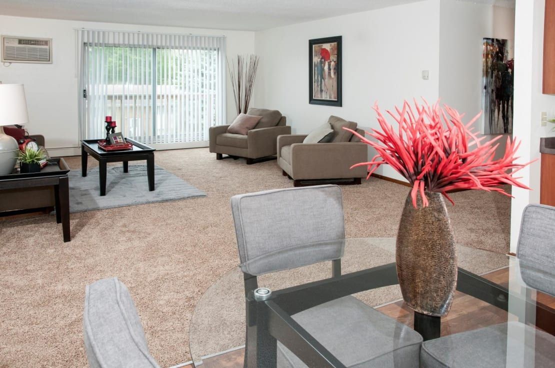 A living room with a dining table and chairs and a vase of flowers on the table.
