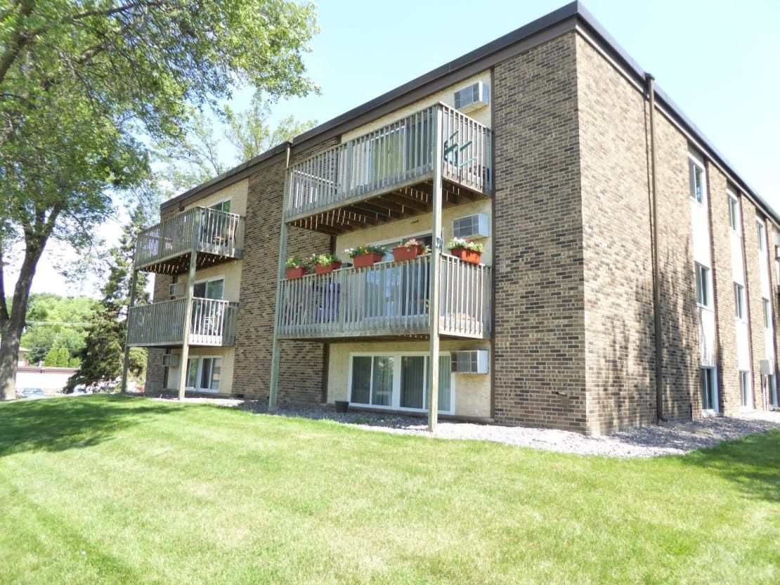 A large brick apartment building with balconies and a lush green lawn in front of it.