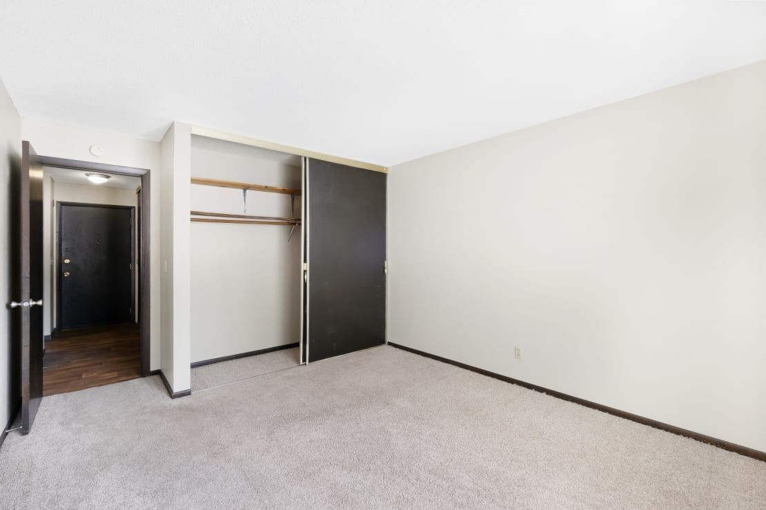 An empty bedroom with a closet and a door leading to a hallway.