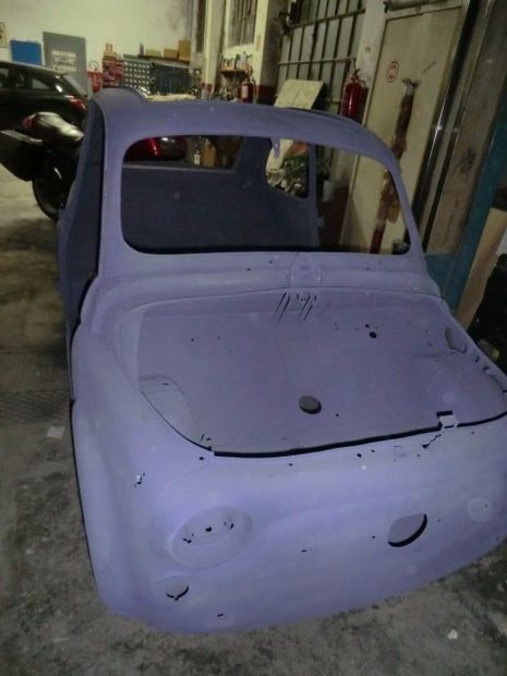 Carrozzeria di un'auto d'epoca con primer viola in un'officina, vista posteriore, senza finestrini e finiture.