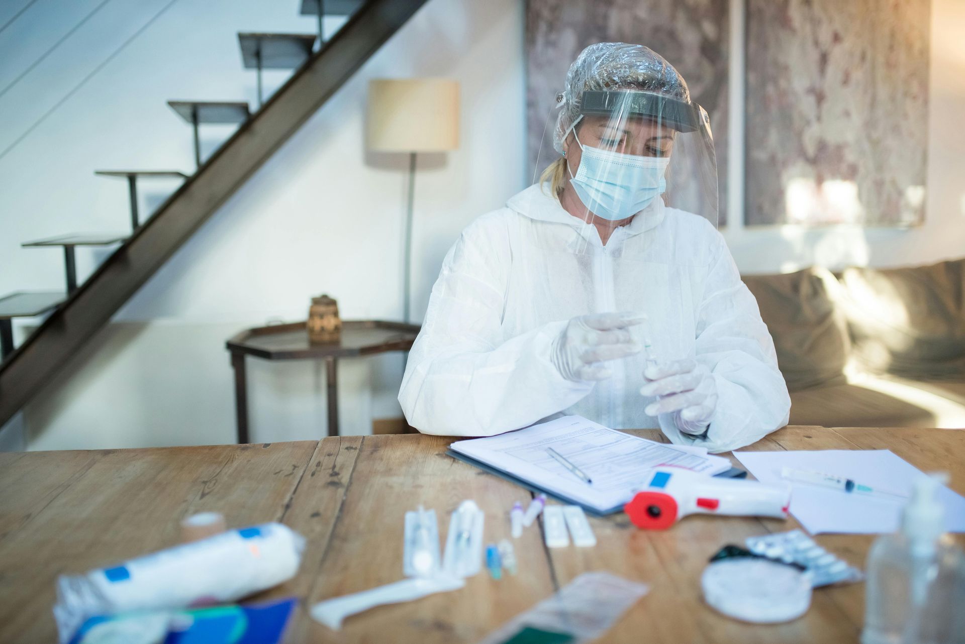A woman in a protective suit and mask is sitting at a table.