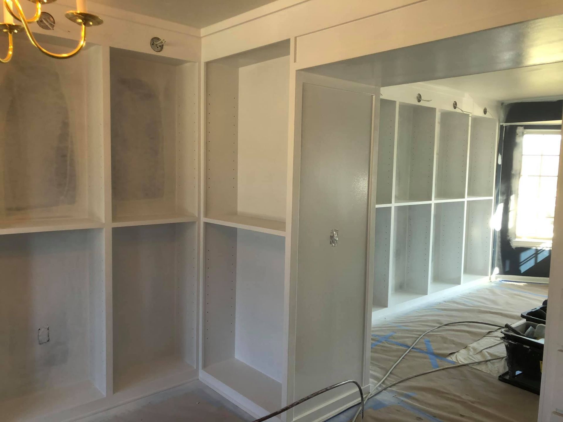 White built-in shelving units under construction in a room, with painting supplies visible on a drop cloth.