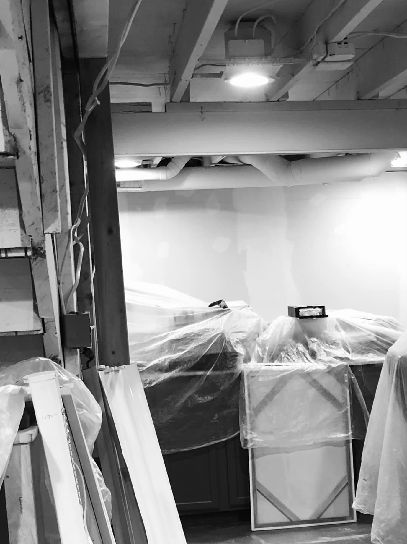 A basement under renovation with walls covered in plastic sheeting and construction materials stored throughout.