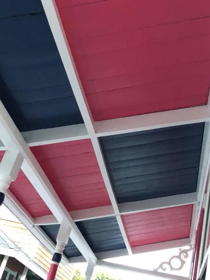 A porch ceiling featuring a grid of wooden panels painted in alternating squares of bright pink and dark navy blue.