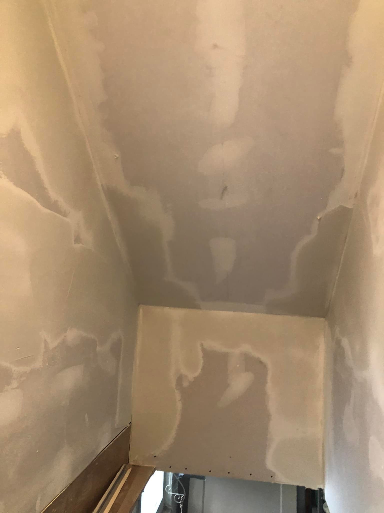 A view looking down a stairwell with unpainted drywall walls and ceiling covered in patches of white joint compound.