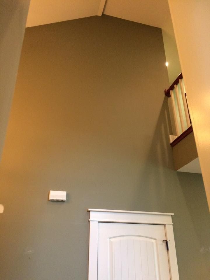 A tall, vaulted wall painted sage green with a white door below and an overlooking balcony with a wooden railing.