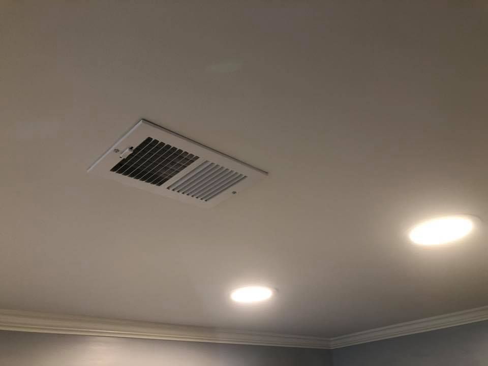A white ceiling with two recessed lights and a rectangular HVAC vent.