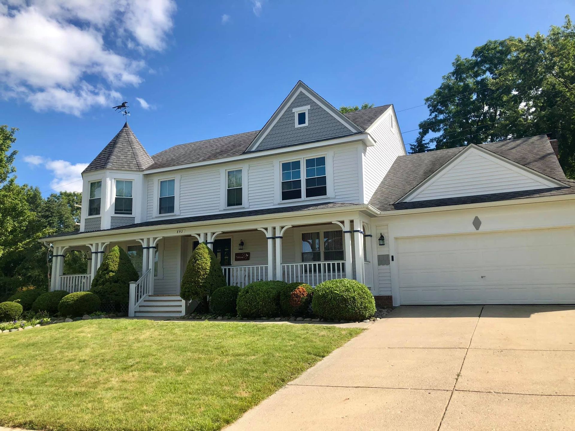 Exterior view of white siding and a stone foundation base above a patch of dark soil next to a brick chimney corner.