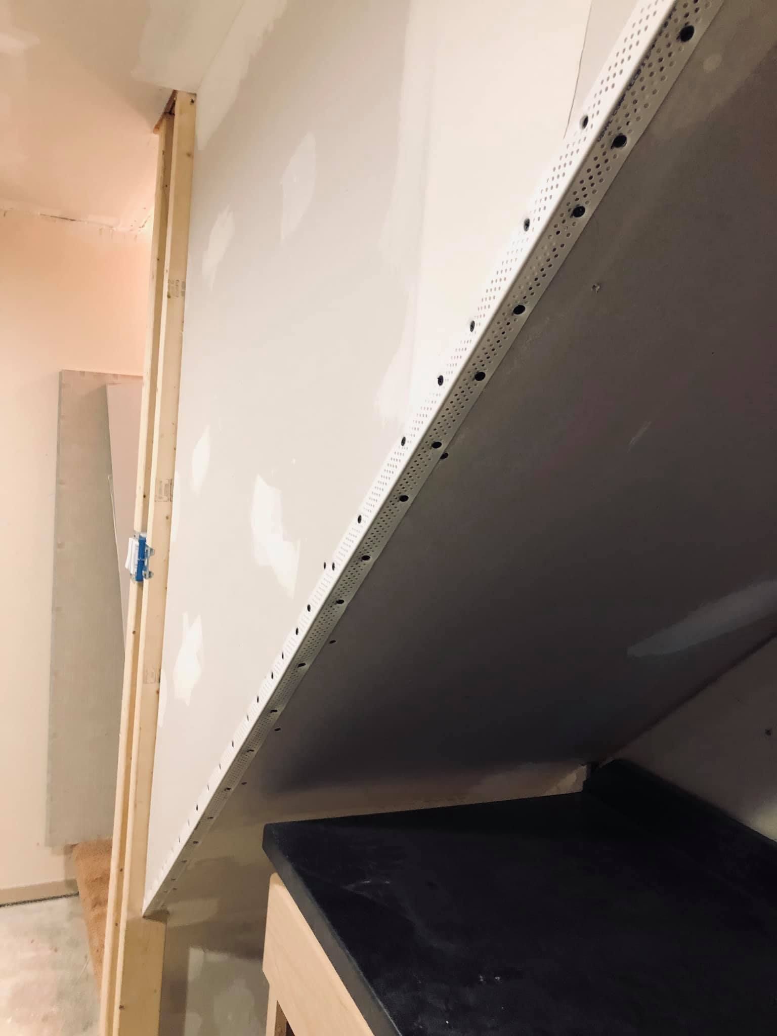 Drywall corner bead installed on the angled edge of a newly framed interior wall in a room under construction.