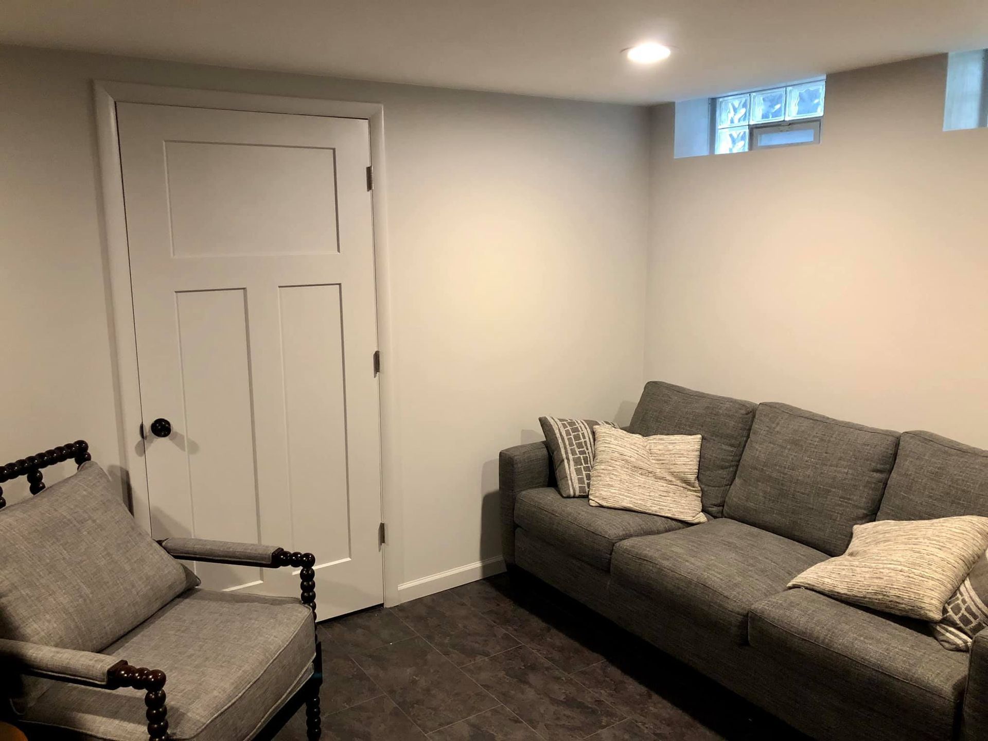 A basement living space featuring a wooden staircase with white railings, a hanging chair, and grey cabinets.