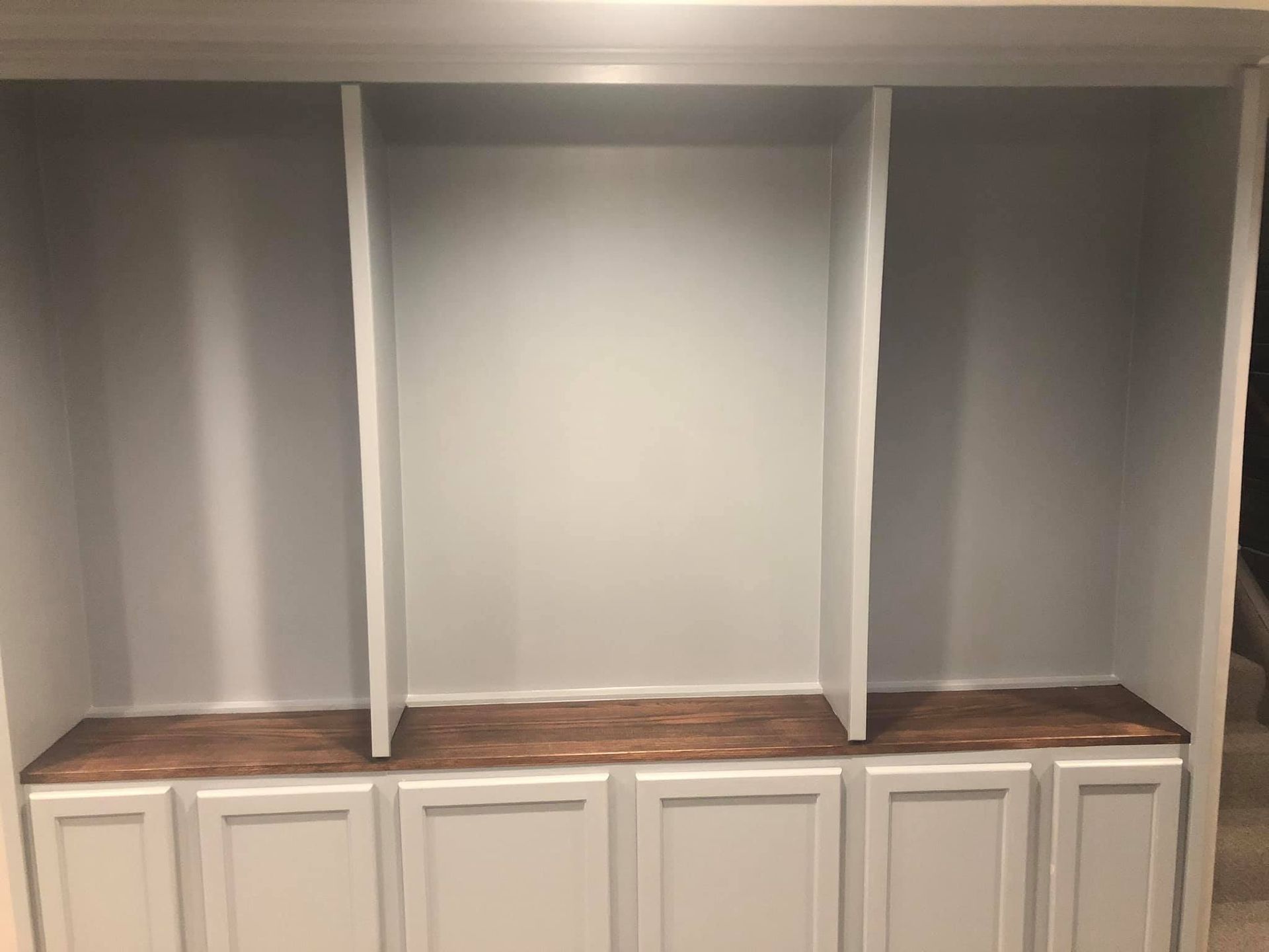Built-in cabinetry with three open shelves above, light gray frame, and stained wood countertops over white cabinets.